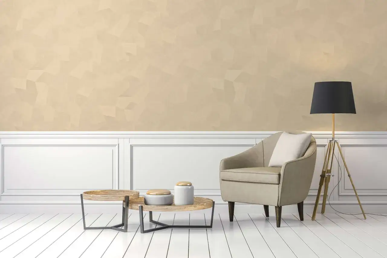 Angolo relax con poltrona beige, tavolini in legno e lampada. Le pareti con brillantini color sabbia creano un'atmosfera luminosa.