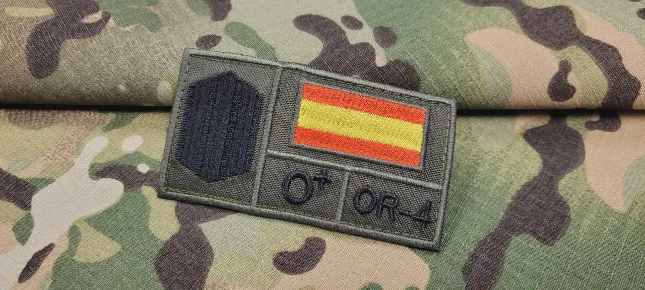 Parches con la bandera de Espa&ntilde;a y el rango OR-4, listos para ser cosidos en un uniforme de camuflaje.