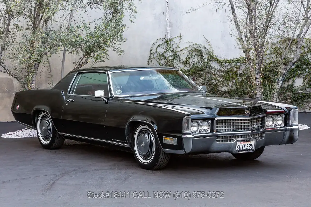 Svart Cadillac Eldorado från 1970, en klassisk amerikansk drömbil, parkerad framför en stenmur med klätterväxter.