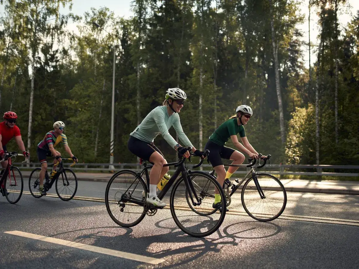 Ciclisti sorridenti su strada asfaltata, immersi nel verde. Un modo sano per alternare bici e camminata, godendosi la natura.
