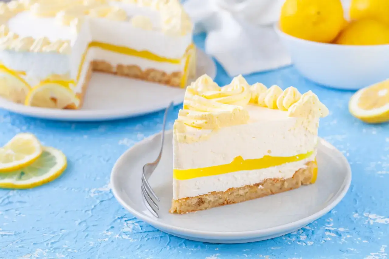 Una fetta di torta fredda al limone, con strati cremosi e una gelatina gialla brillante, decorata con panna montata e limone.