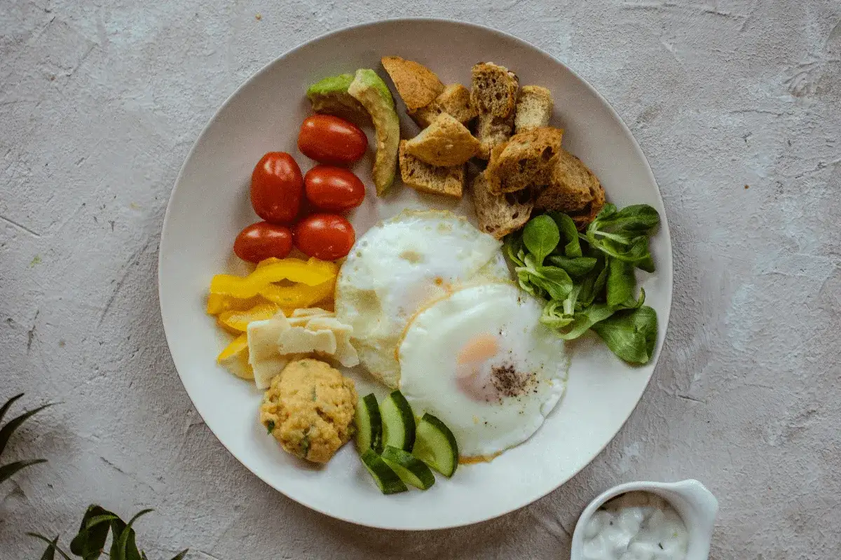 Talerz z jajkami sadzonymi, pomidorkami, awokado, grzankami i warzywami. Idealny na śniadanie w stylu dieta jajeczna.
