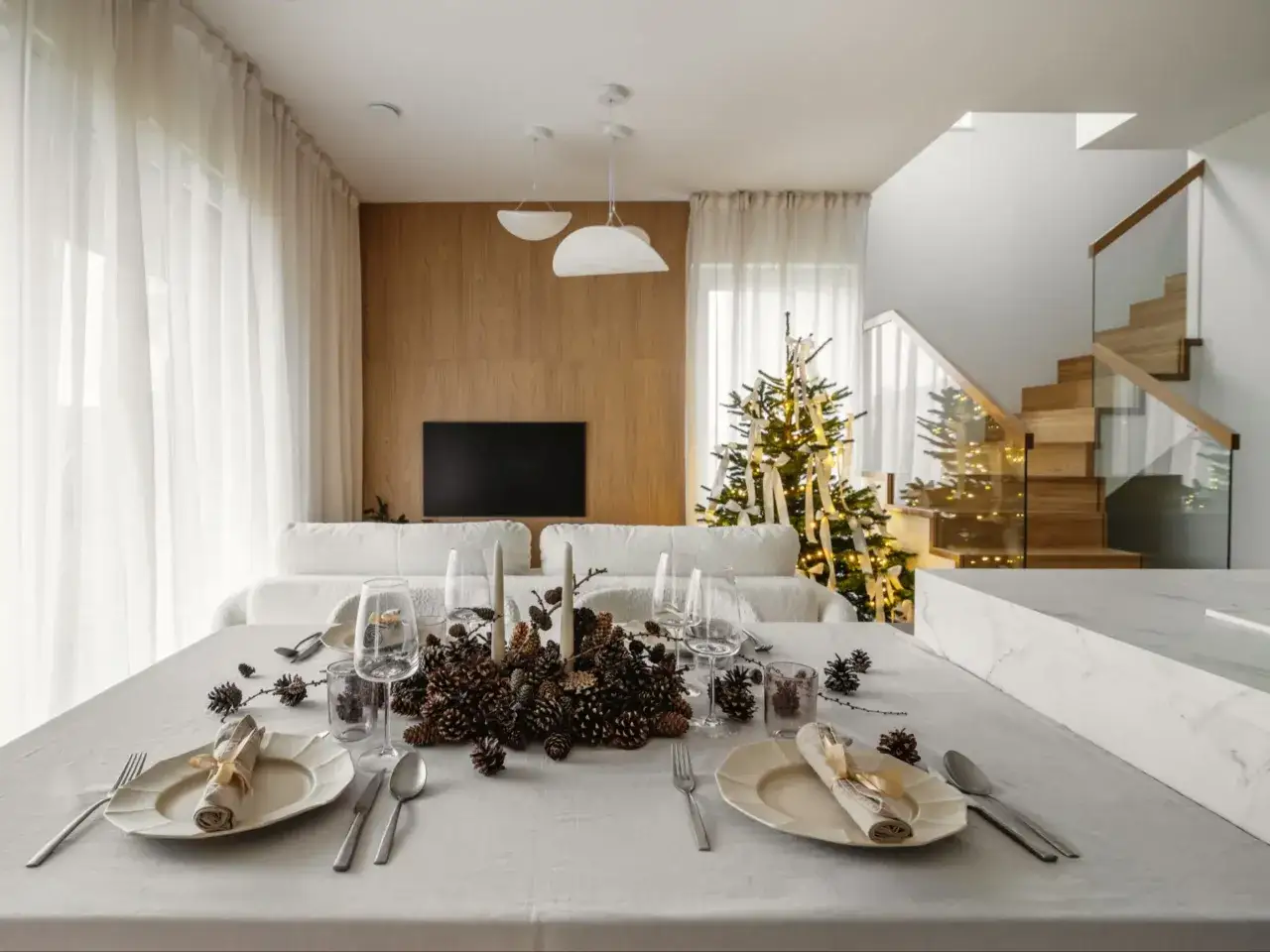Stół nakryty do kolacji, ozdobiony szyszkami i świecami, w tle choinka i schody. To kwintesencja quiet luxury.