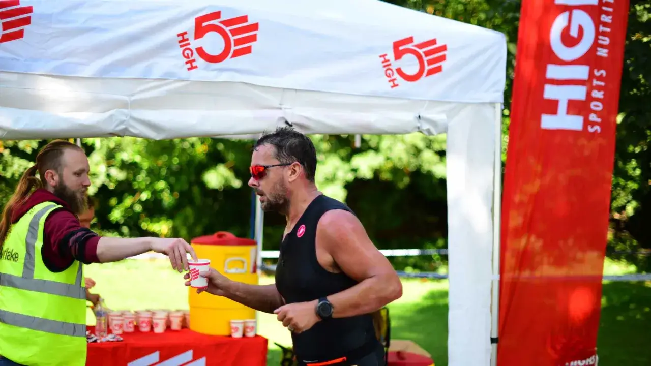 Zawodnik triathlonu otrzymuje kubek z napojem energetycznym od wolontariusza.