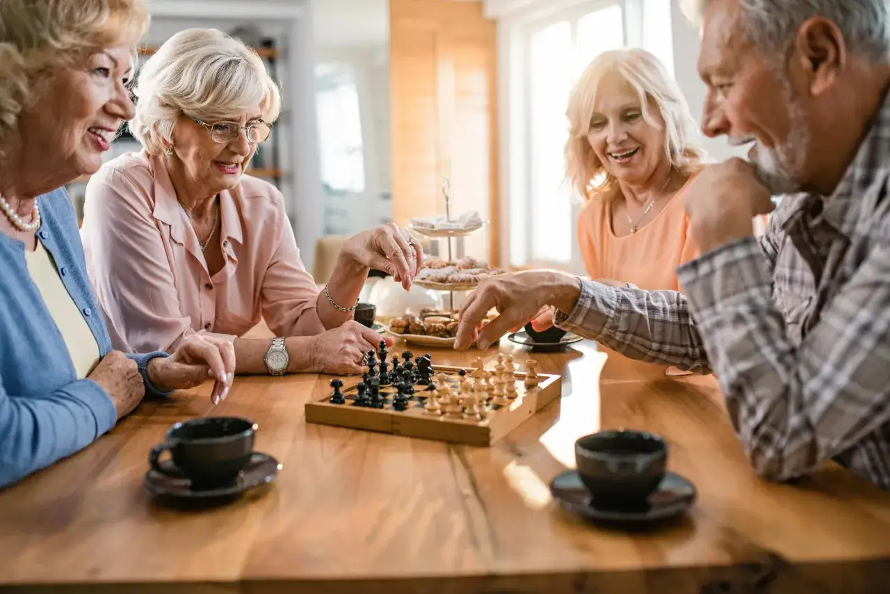 Quatre amis profitent d'un jeu d'&eacute;checs, un excellent exercice de m&eacute;morisation, autour d'une table en bois avec des tasses de caf&eacute; et des biscuits.