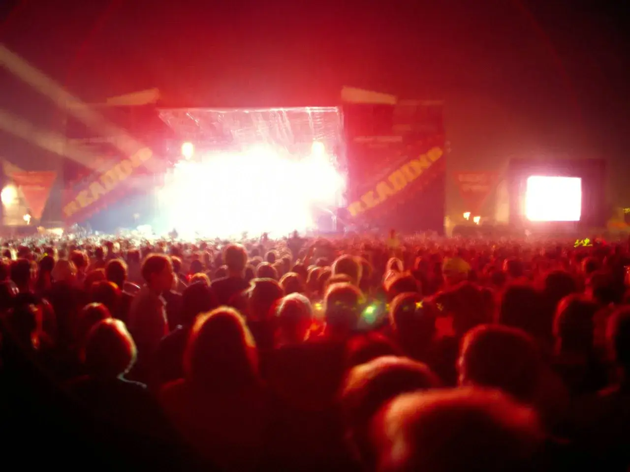 Tłum ludzi na koncercie nu metalowym, rozświetlony czerwonymi światłami i jasną sceną.