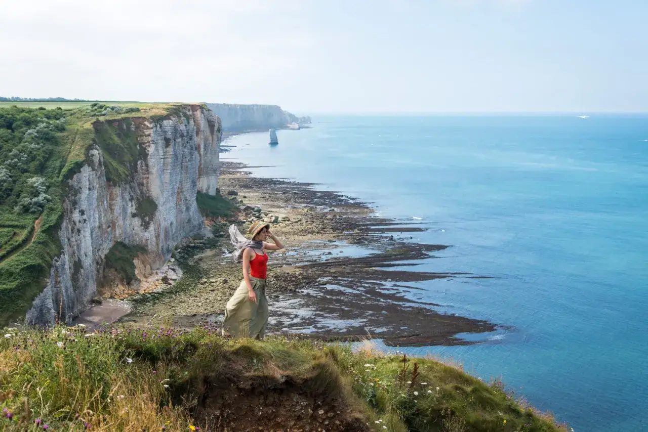 Une femme admire le paysage côtier, entre falaises et mer, rappelant la beauté d'Étretat et de la Baie de Somme.