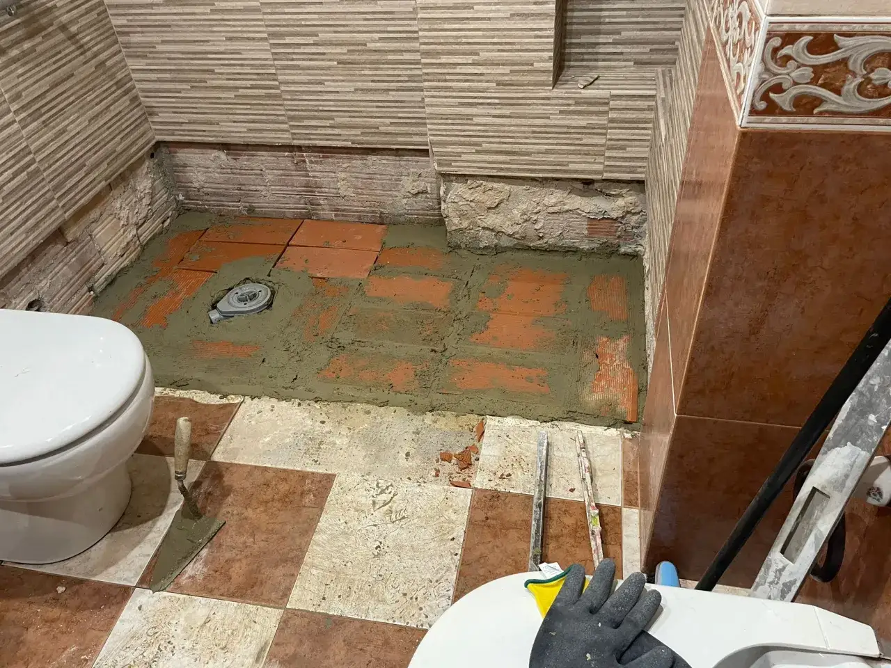 Ba&ntilde;o en obra con inodoro, baldosas rotas y un desague plano reci&eacute;n instalado sobre cemento fresco.