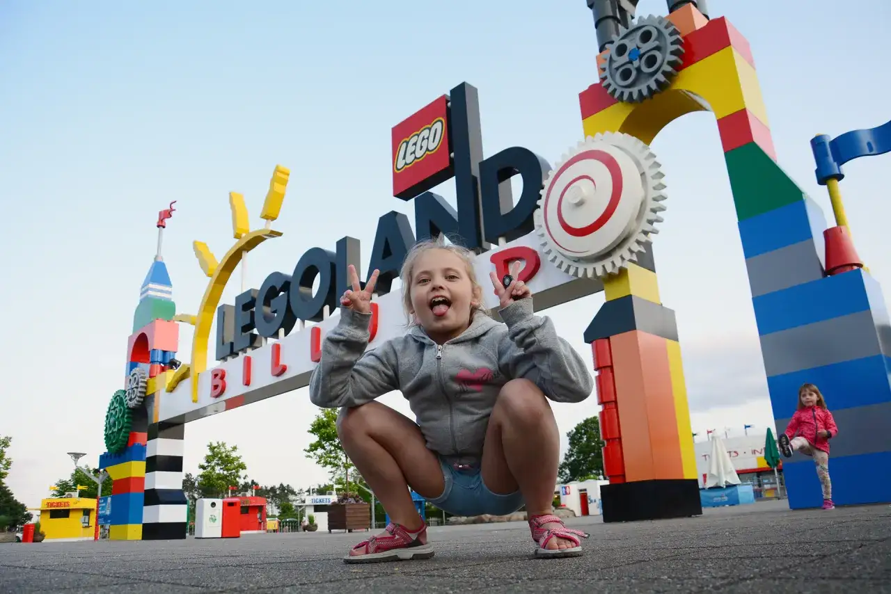 Wesoła dziewczynka pozdrawia przed bramą Legolandu. Czy to Legoland Niemcy czy Dania?
