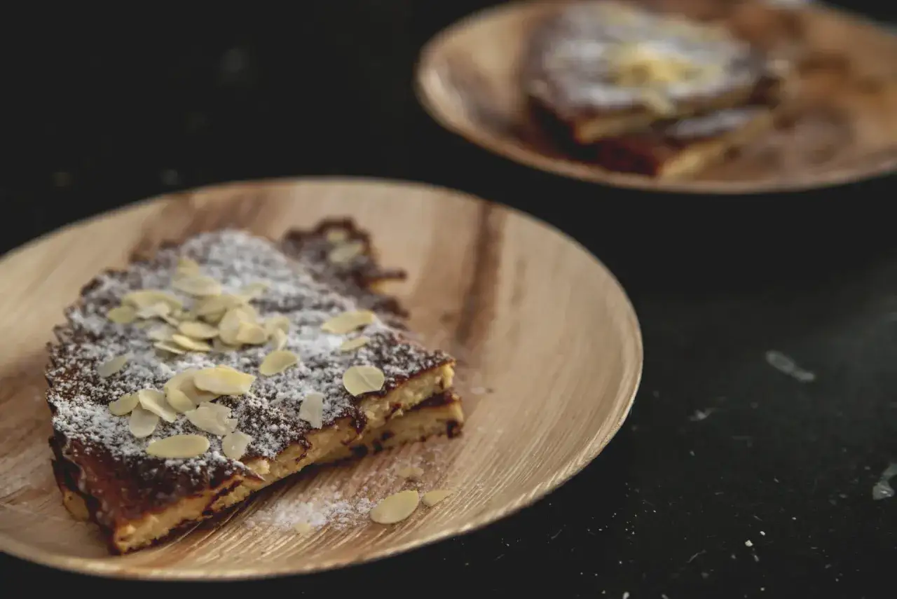 Słodki keto omlet z płatkami migdałów i cukrem pudrem na drewnianym talerzyku. Pyszny deser dla każdego.
