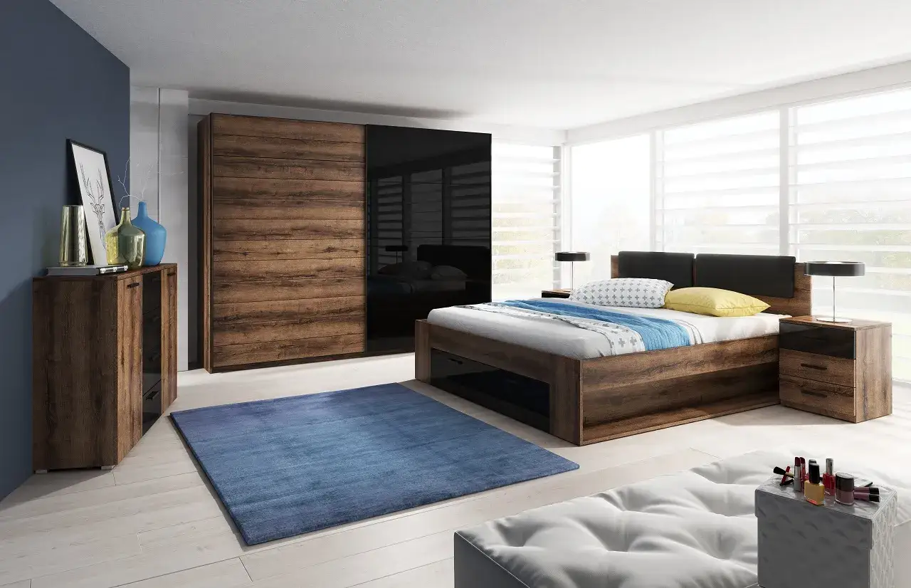Habitaci&oacute;n con poca luz, cama de madera oscura, armario con puertas de madera y cristal negro, alfombra azul y mesitas de noche.