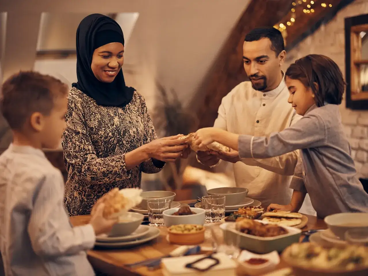 Familie teilt Brot beim Zuckerfest. Die Mutter im Hijab reicht es dem Sohn, w&auml;hrend die Tochter es vom Vater nimmt.