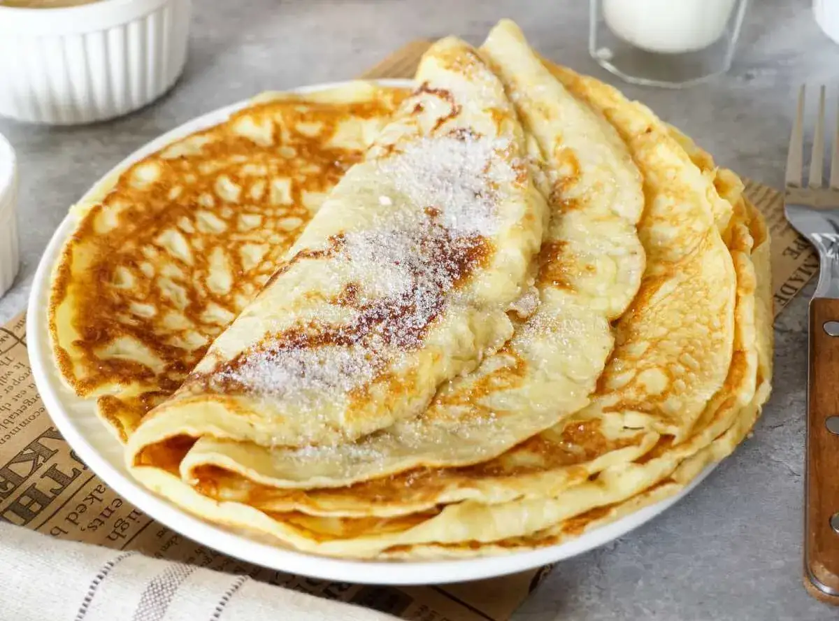 Ein Stapel goldbrauner Pfannkuchen, bestreut mit Zucker. Ein einfaches Pfannkuchen Rezept für jeden Tag.