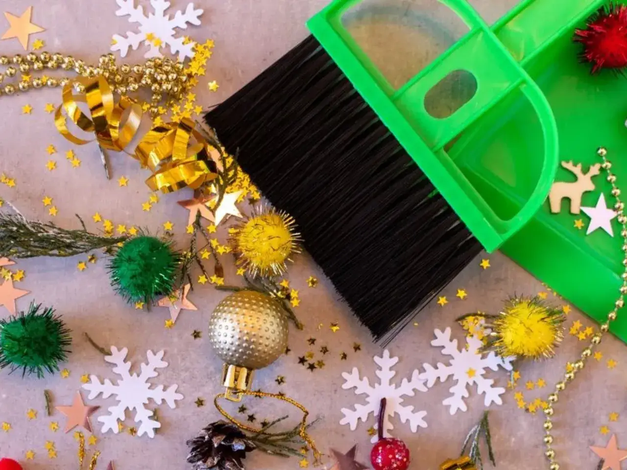 Een groene stoffer en blik vegen kerstversiering op: glittersterren, kerstballen, sneeuwvlokken en slingers. Het is tijd voor het opruimen van kerstspullen.