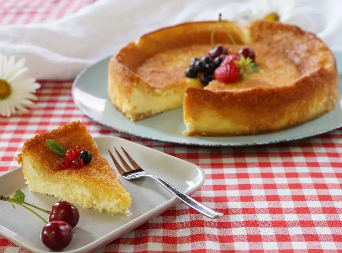 Ein St&uuml;ck vom dreh dich um Kuchen mit Beeren und Kirschen auf einem Teller. Der ganze Kuchen steht im Hintergrund.
