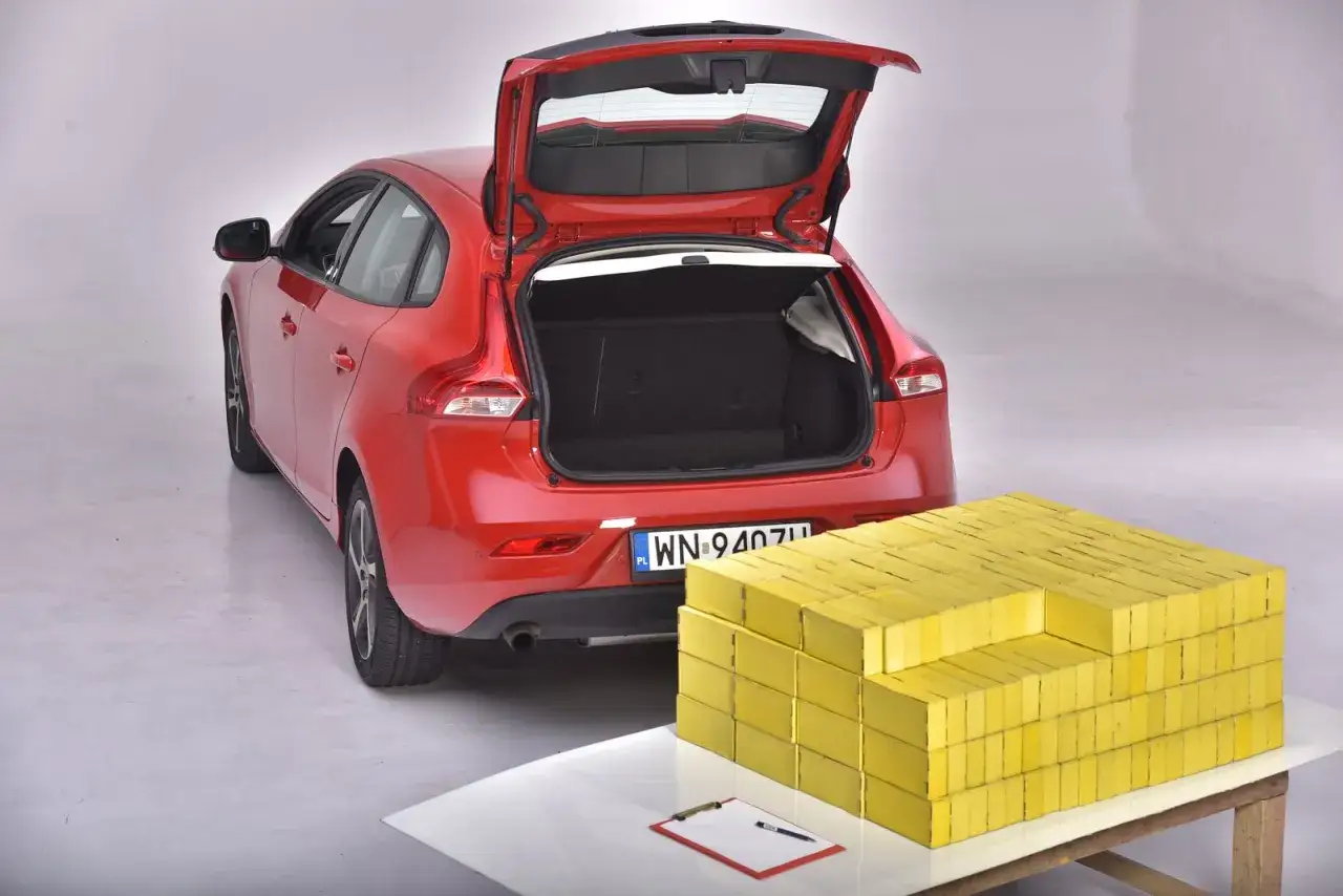 Czerwony hatchback z otwartym bagażnikiem obok sterty żółtych cegieł. Czy zmieści się wszystko, co potrzebne, jak w sedanie?