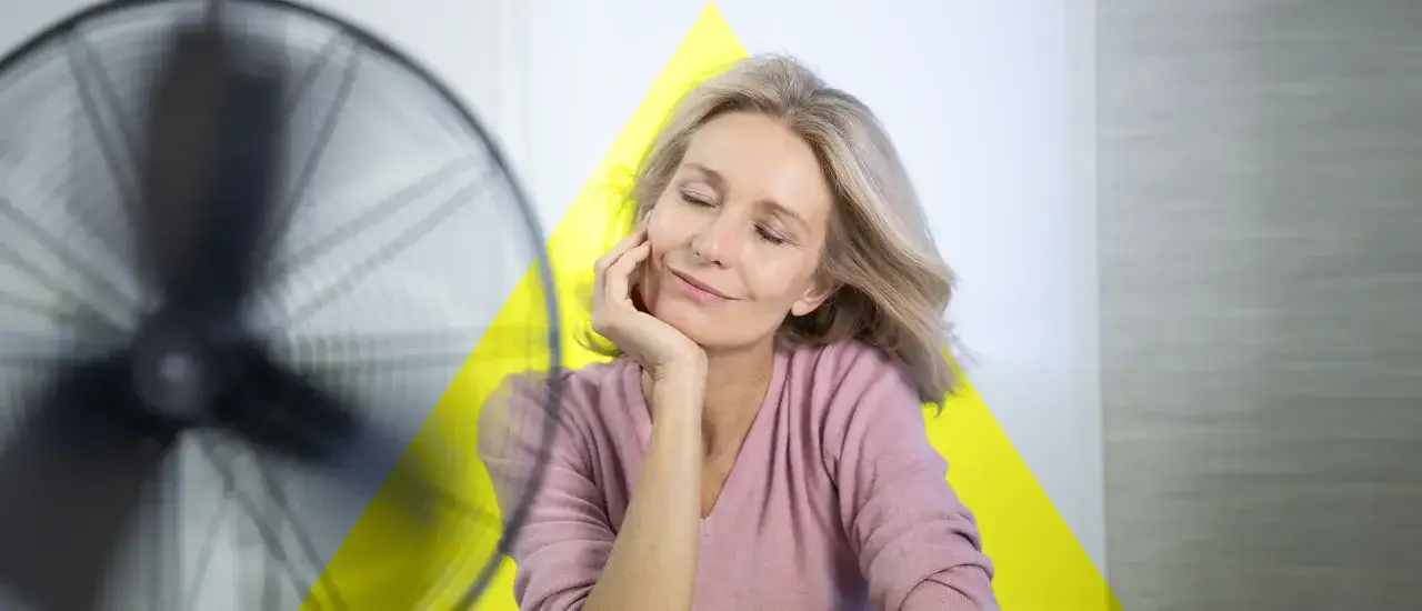 Frau genießt kühle Brise vom Ventilator. Hitzewallungen ohne Wechseljahre? Abkühlung tut gut.