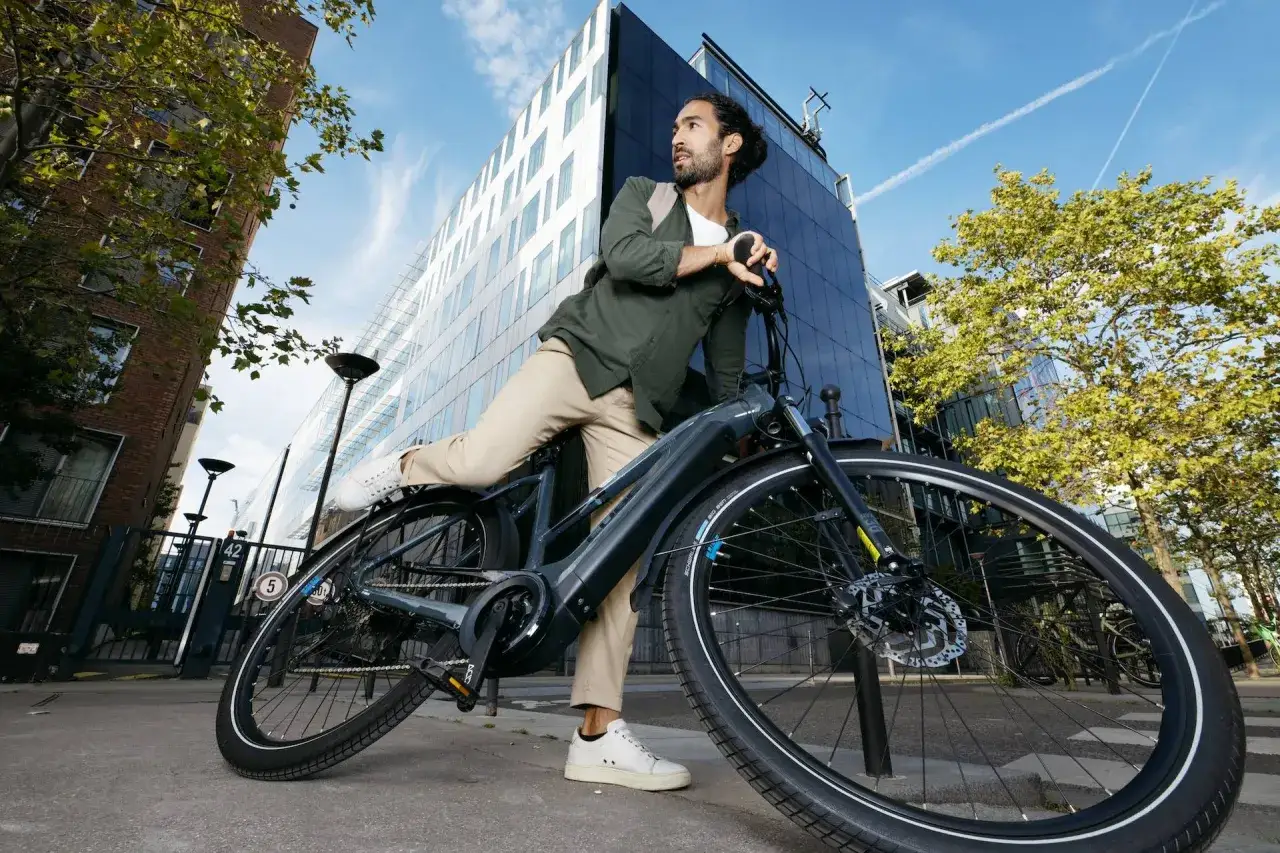 Man met rugzak haalt accu uit elektrische fiets, klaar voor een stedentrip.