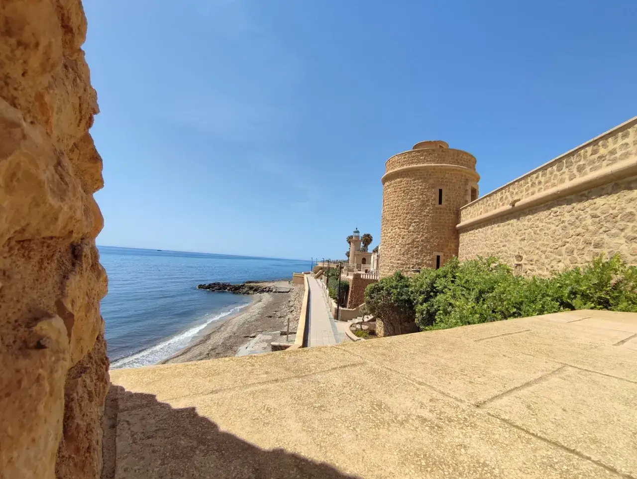 Torreón y faro en el paseo marítimo de Roquetas de Mar, con el mar azul y el cielo despejado.