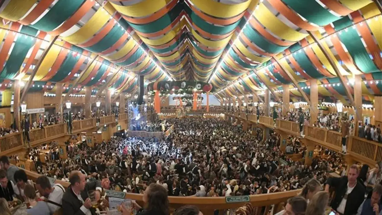 Ein riesiges Festzelt beim bayern oktoberfest, gef&uuml;llt mit tausenden feiernden Menschen unter bunten Stoffbahnen.