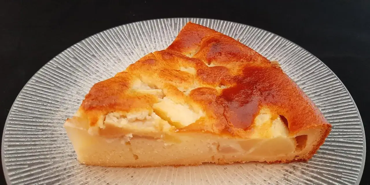 Tranche de clafoutis aux poires, dor&eacute;e et moelleuse, servie sur une assiette transparente aux reflets givr&eacute;s.