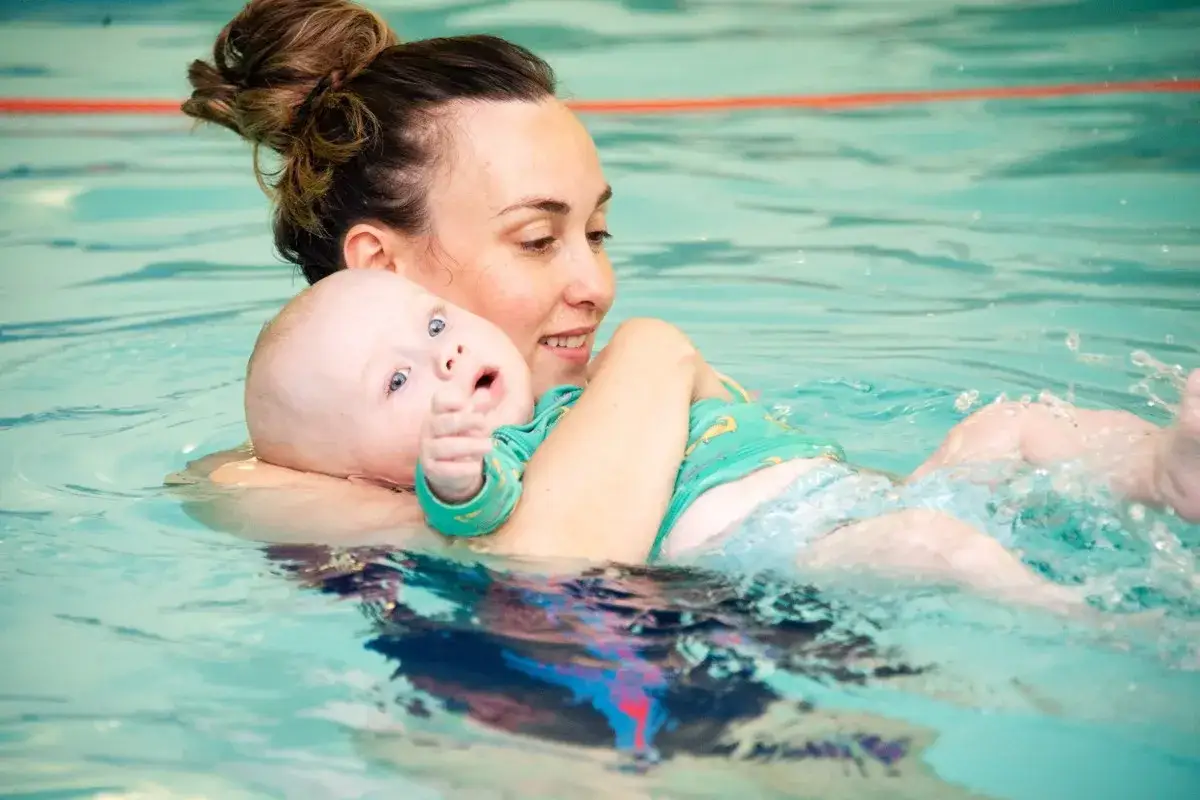Mommy and me swim classes: A mom smiles as she holds her baby, who looks surprised, in the pool.