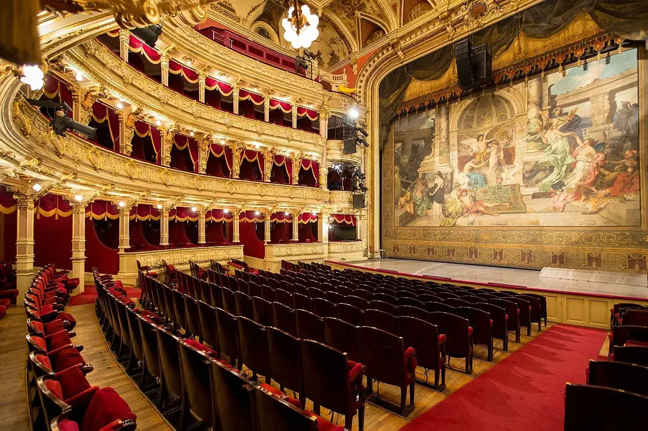 Wnętrze teatru z czerwonymi lożami i malowidłem na scenie. Idealne miejsce, by przeżyć co to dramat romantyczny.
