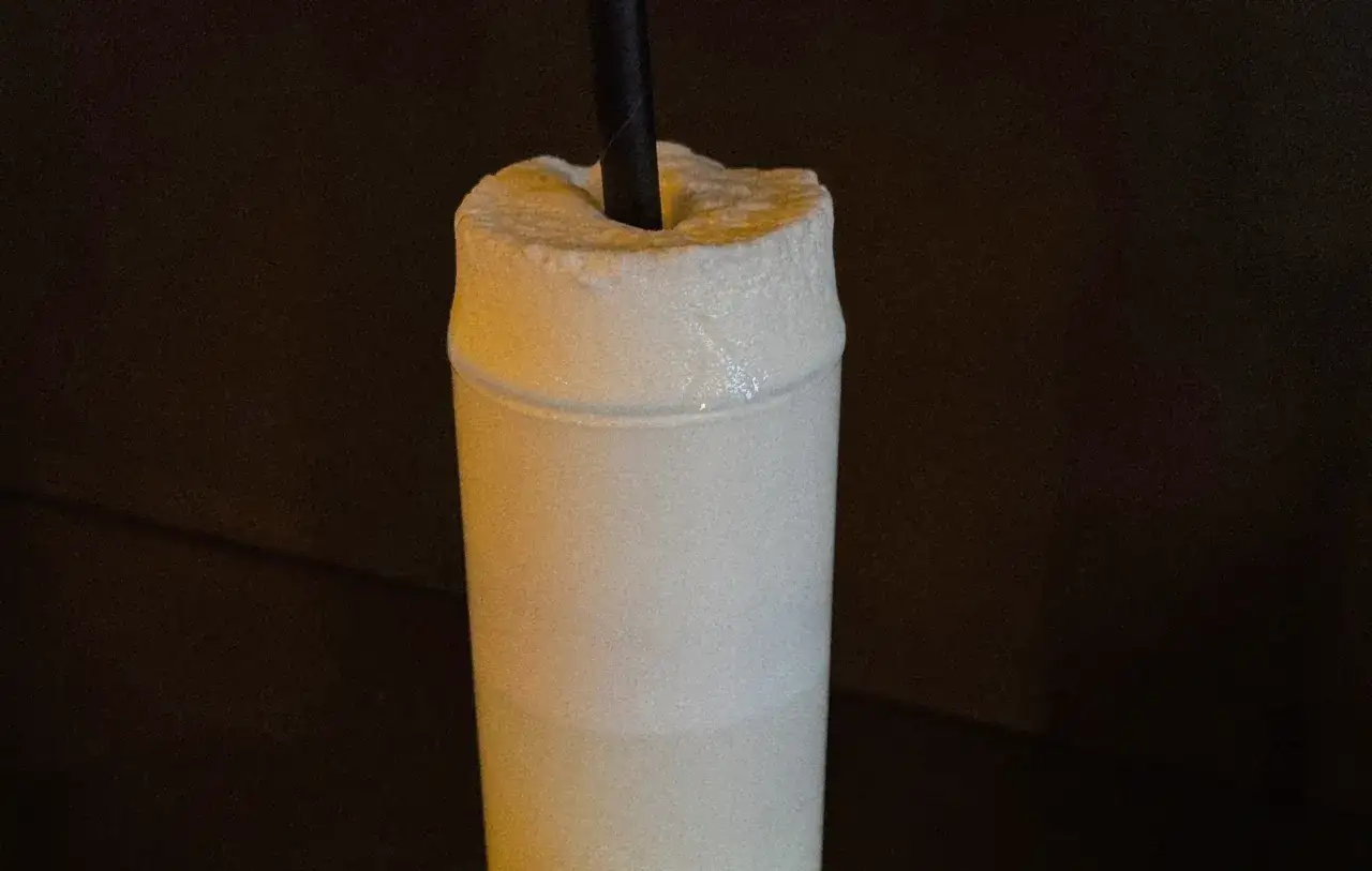 Ein cremiger Ramos Gin Fizz mit einem schwarzen Strohhalm, der aus dem &uuml;ppigen Schaum ragt.