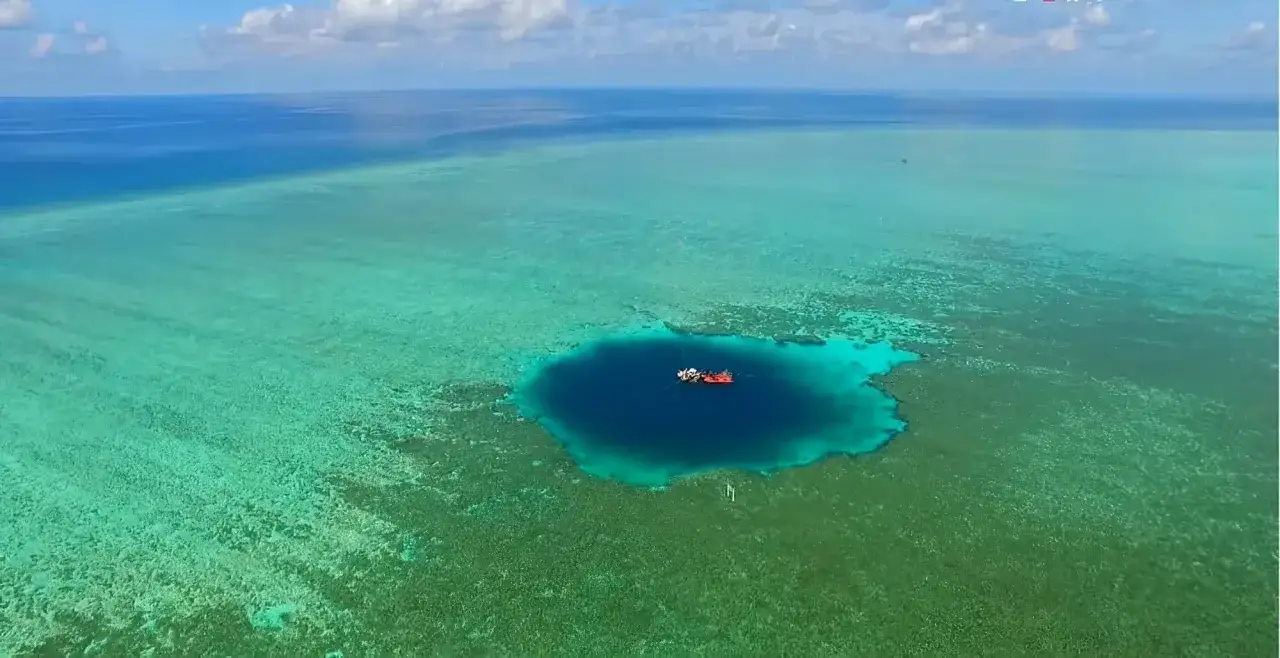 Un bateau rouge et blanc flotte au-dessus du trou du dragon, un abîme bleu profond entouré de récifs coralliens turquoise.