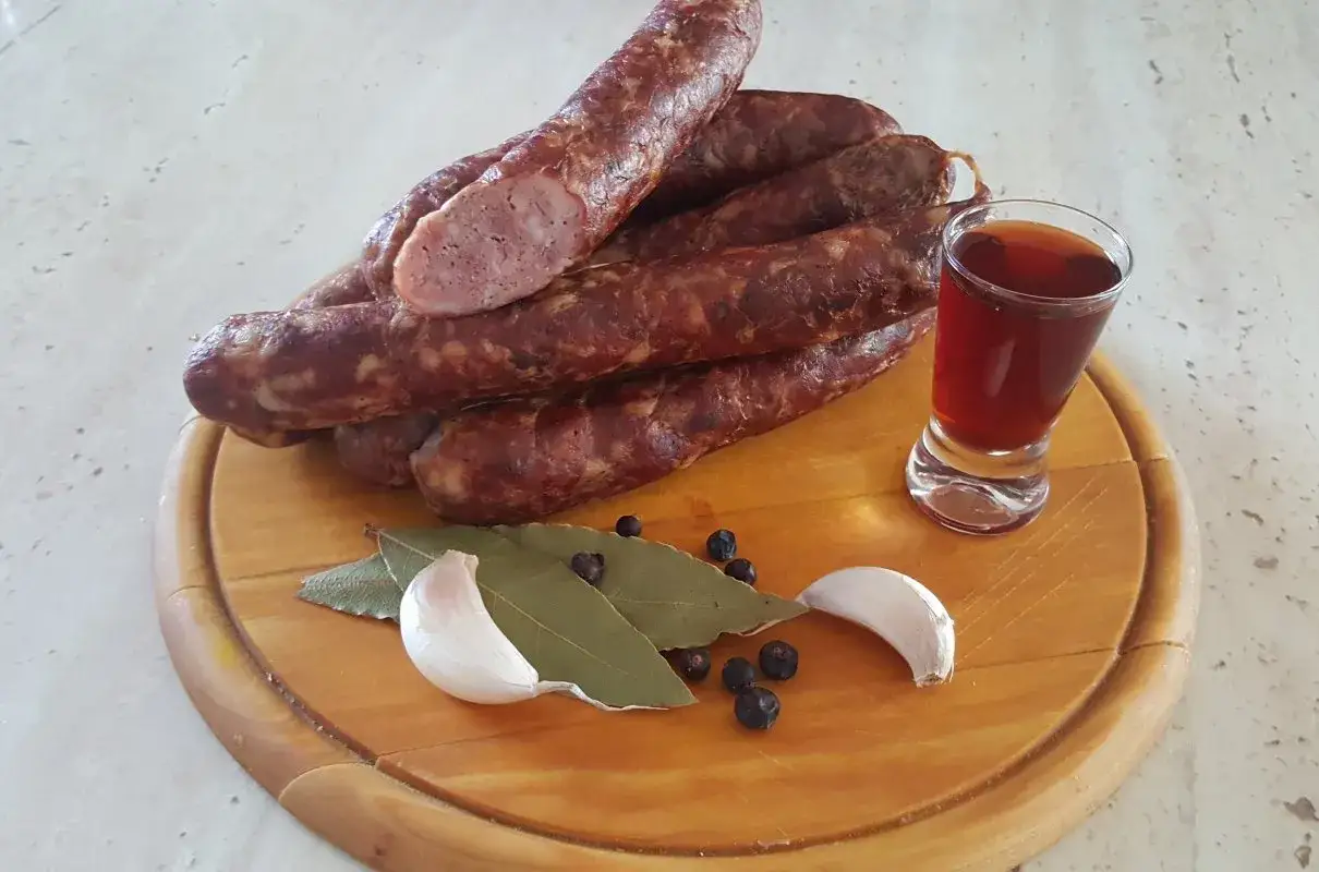 Kiełbasa polska surowa przepis: aromatyczne wędliny, czosnek, liście laurowe i jałowiec na desce. Idealne na tradycyjny posiłek.