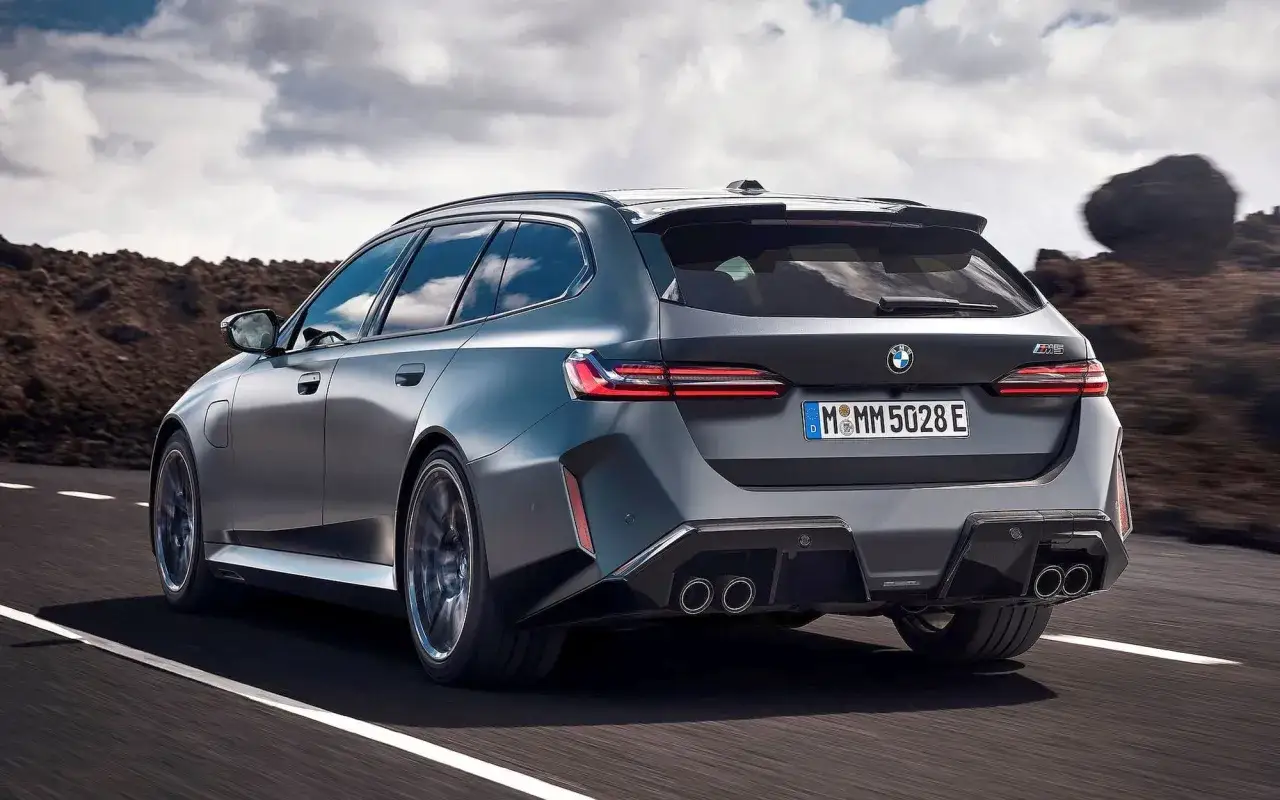 Szary BMW M5 Touring pędzi po drodze, ukazując swoje sportowe linie i cztery końcówki wydechu.