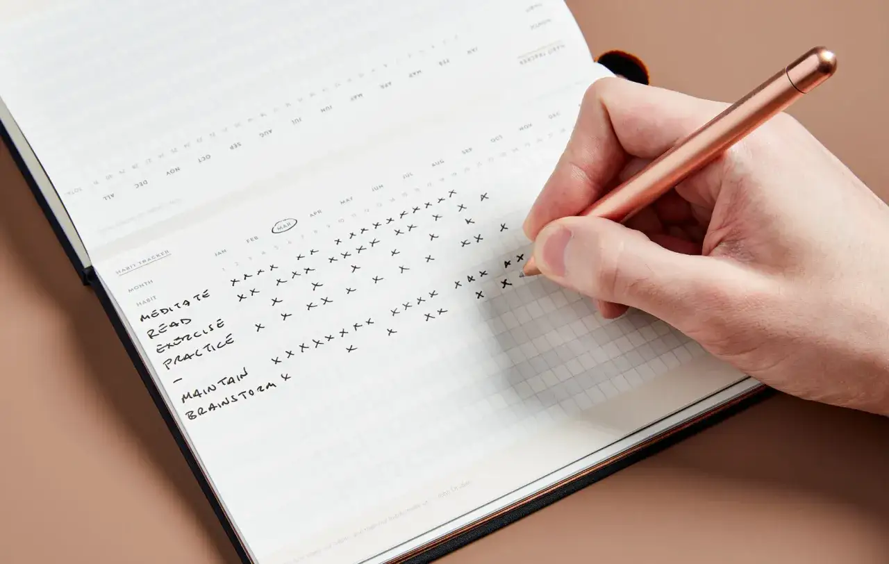 Tracking habits like meditating and reading is a great way to learn how to change your behavior. A hand marks progress on a habit tracker.