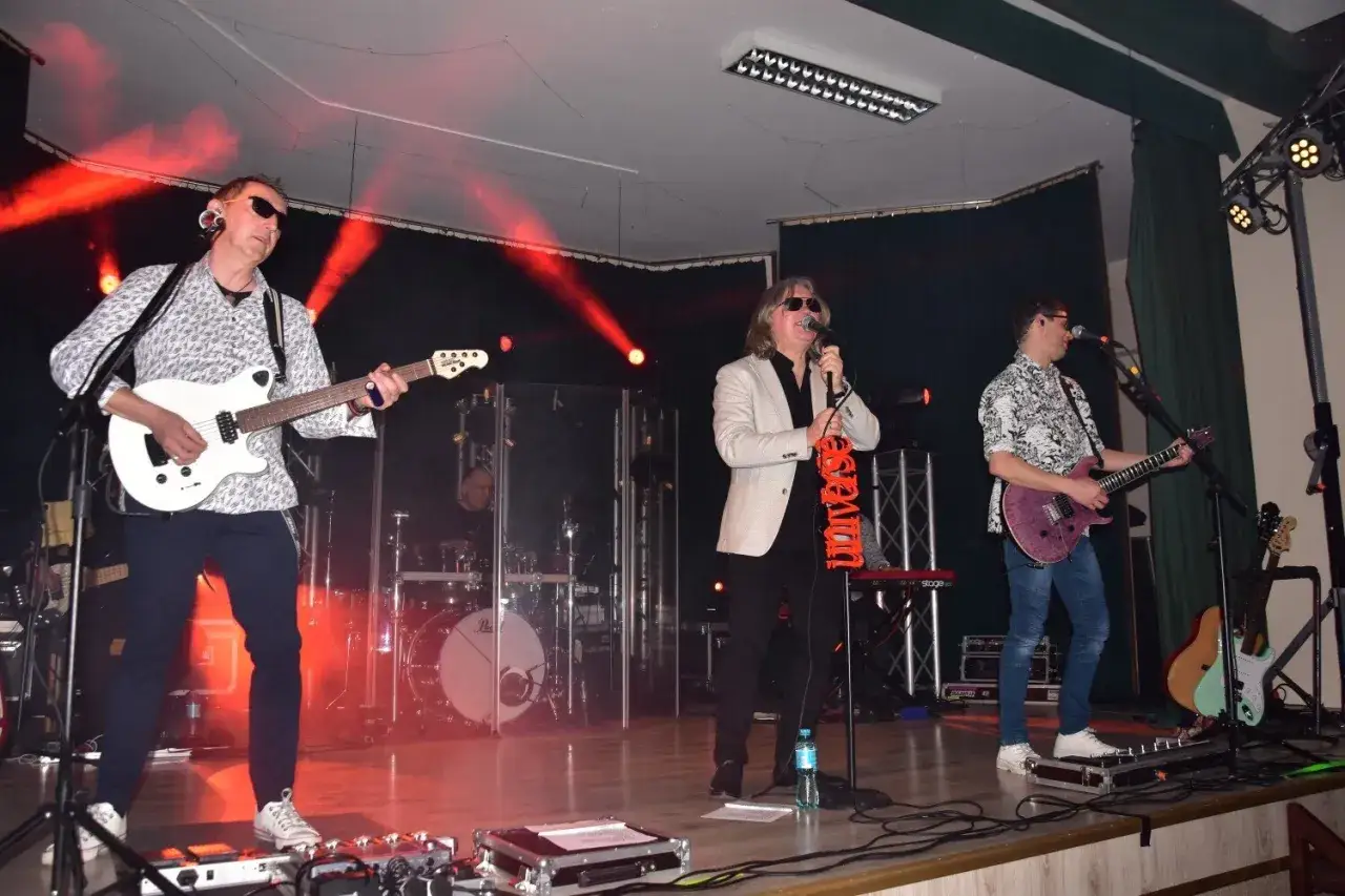 Zespół Universe na scenie, gitarzyści i wokalista w okularach przeciwsłonecznych, czerwone światła.