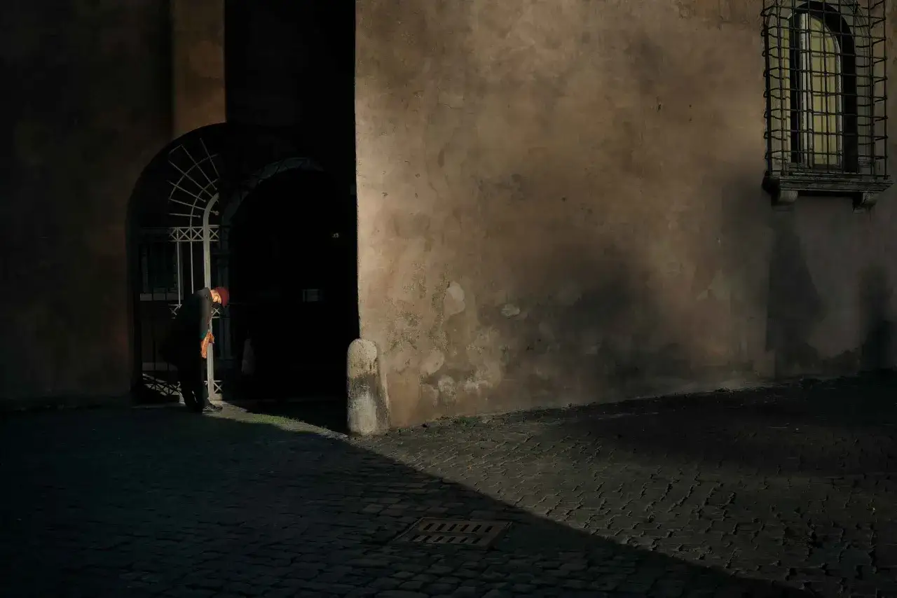 Un uomo con cappello rosso si china sotto un arco in un vicolo romano. #streetphotography