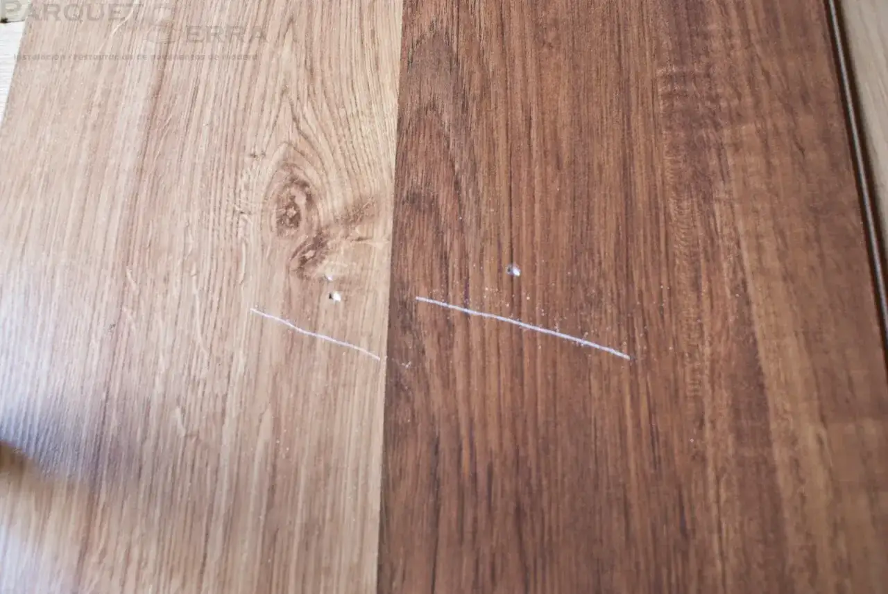Dos tablones de parquet, uno claro y otro oscuro, muestran arañazos blancos. Busca remedios caseros para reparar parquet y devolverle su brillo.