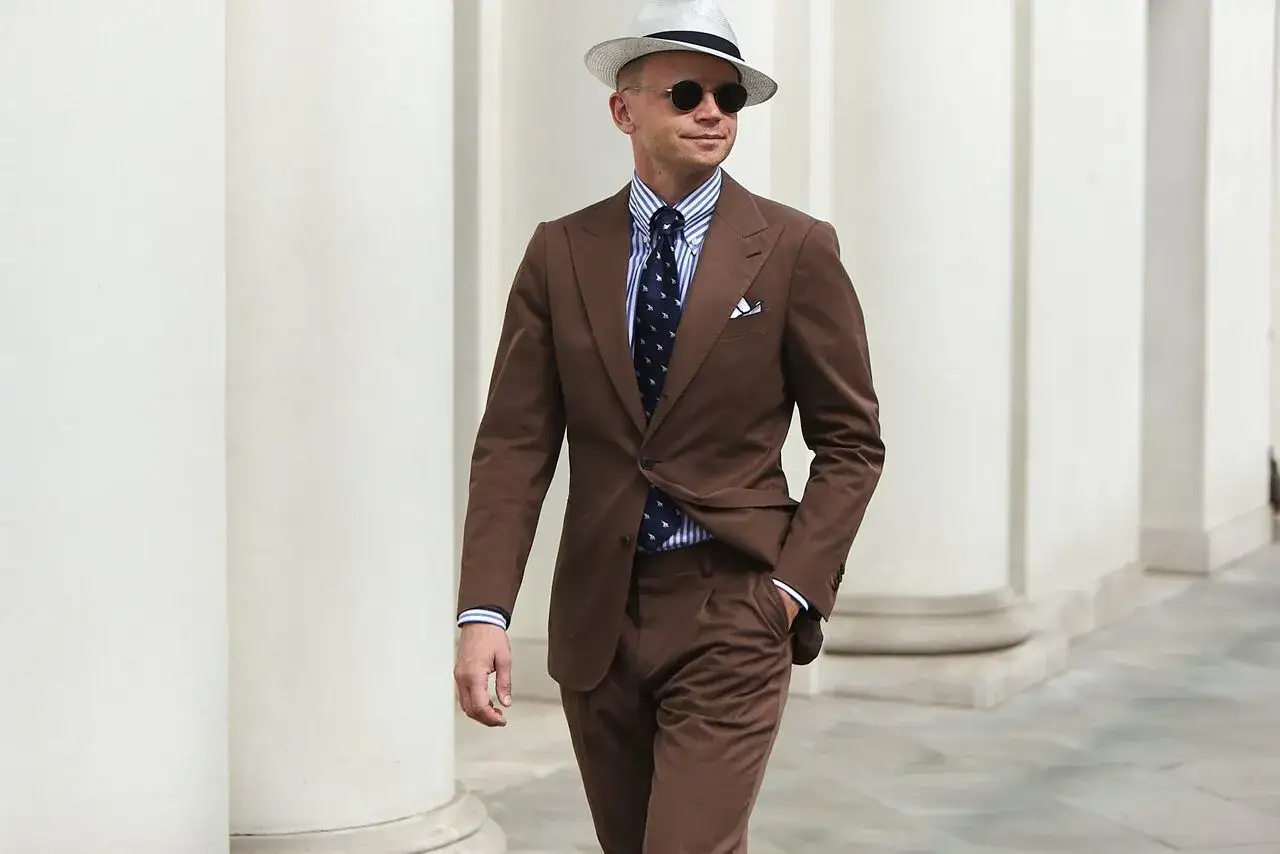 Elegancki mężczyzna w garniturze w kolorze mocca, białej koszuli w paski i kapeluszu.