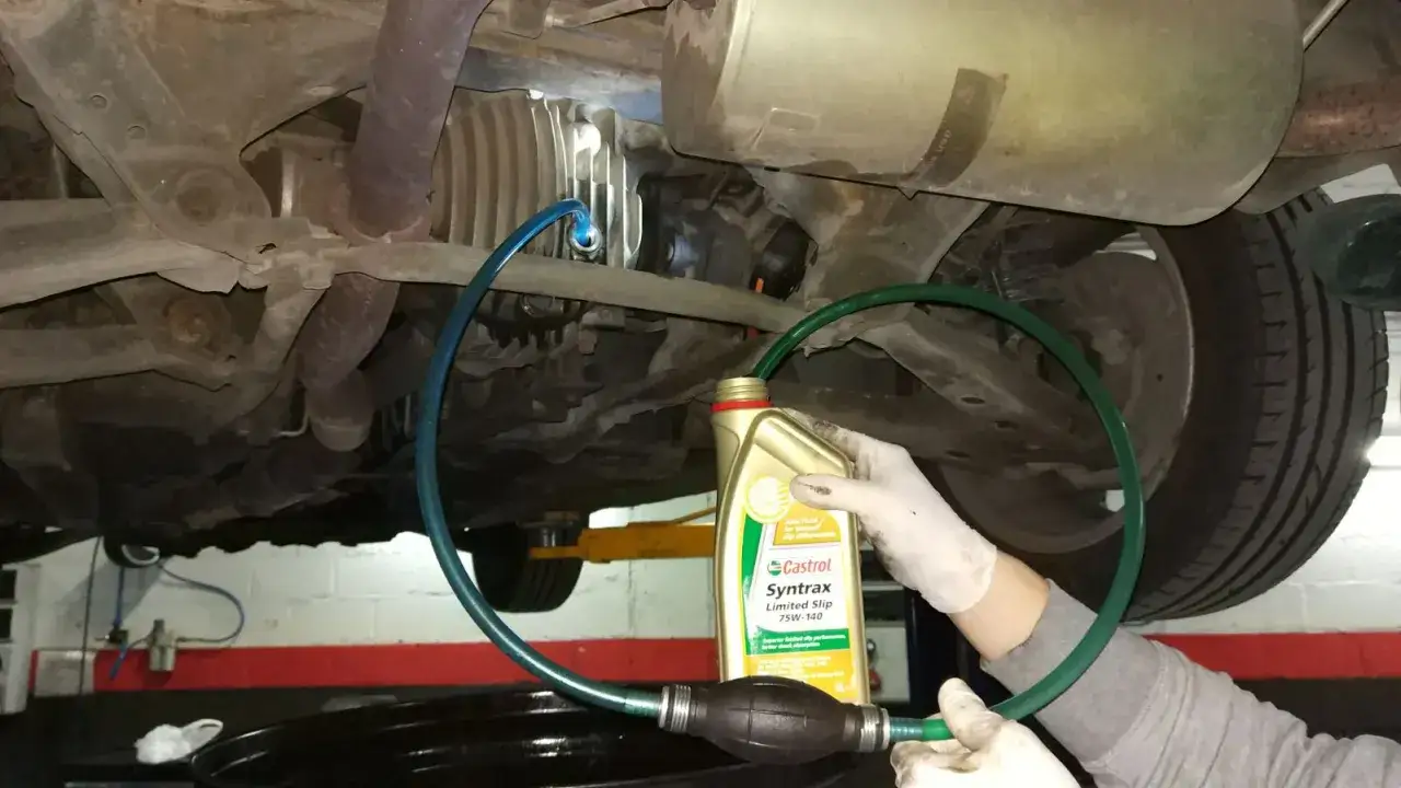 Mano con guante usa bomba para rellenar valvulina caja cambios de un coche.
