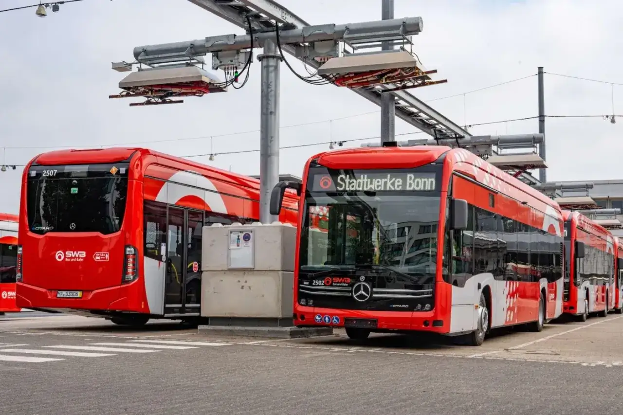 Rote elektrische Busse der Stadtwerke Bonn laden unter Oberleitungen.