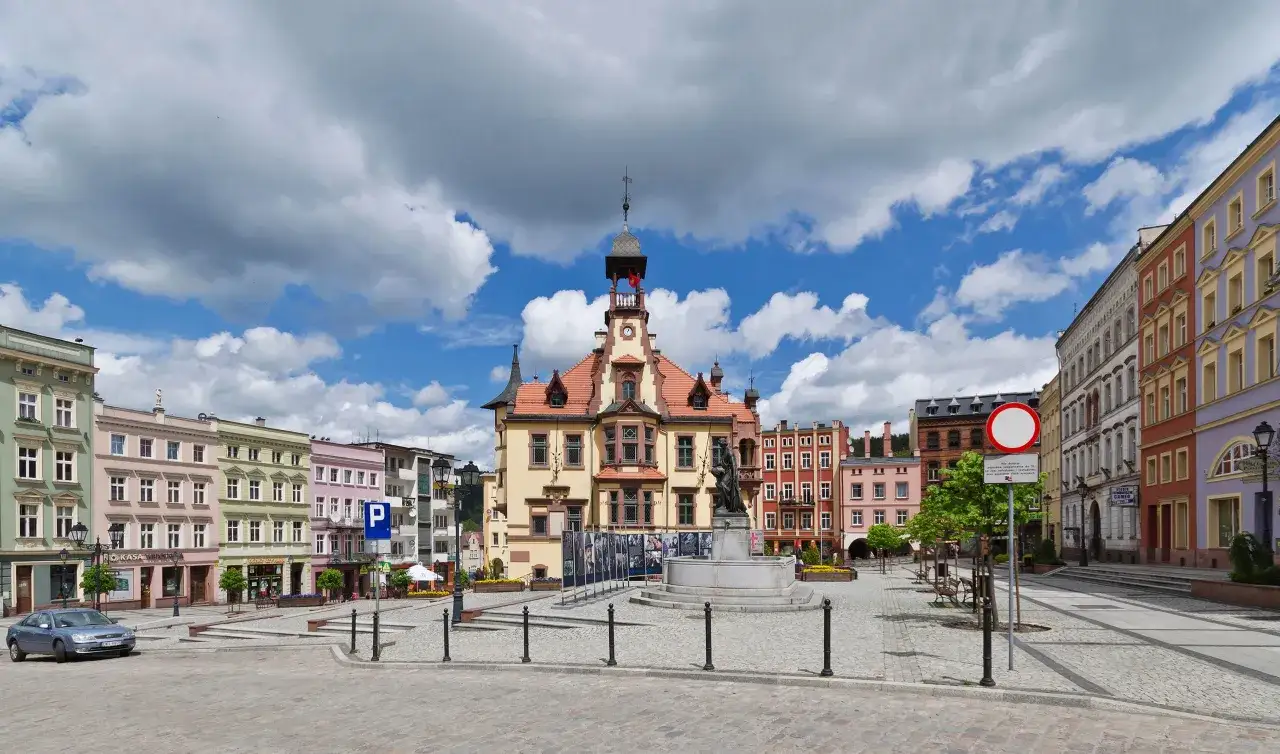 Kolorowe kamienice i ratusz na rynku w Nowej Rudzie. Fontanna ze rzeźbą i wystawa plenerowa.