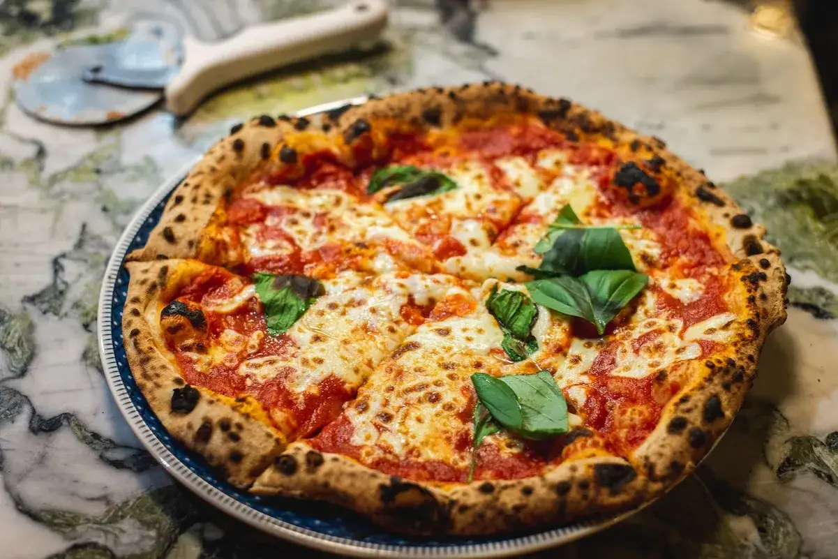 Une délicieuse margarita pizza, avec sa croûte dorée et ses feuilles de basilic frais, prête à être dégustée.
