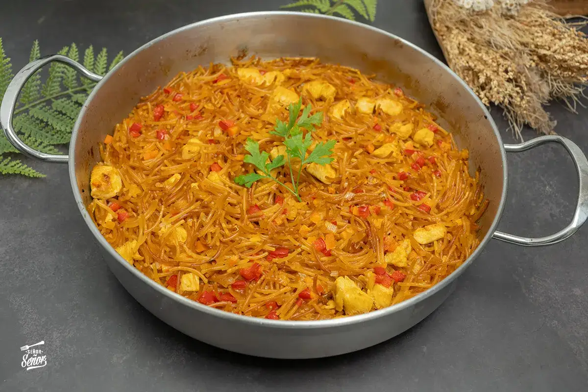Fideuà de pollo en paellera, con fideos finos, trozos de pollo, pimiento rojo y perejil.