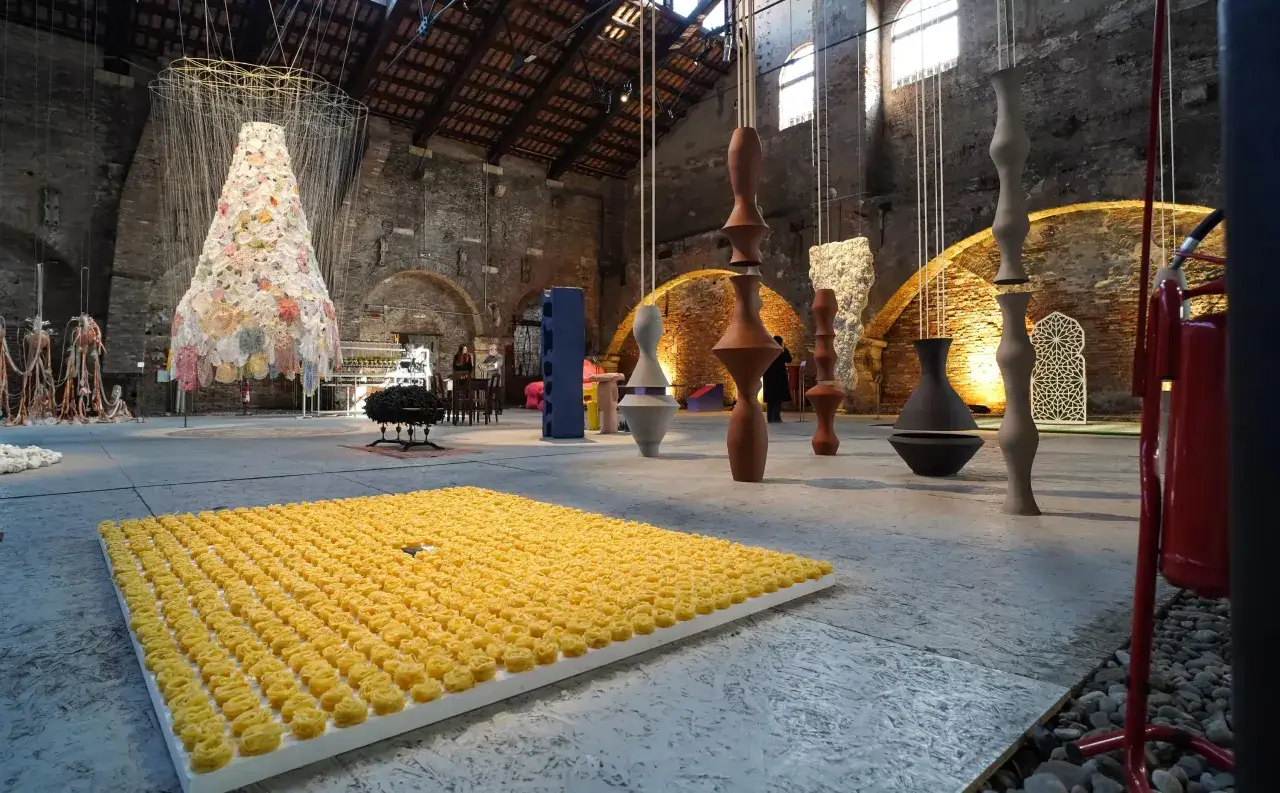 Installazione artistica a Venezia: un tappeto di pasta gialla e sculture sospese in un'antica struttura.