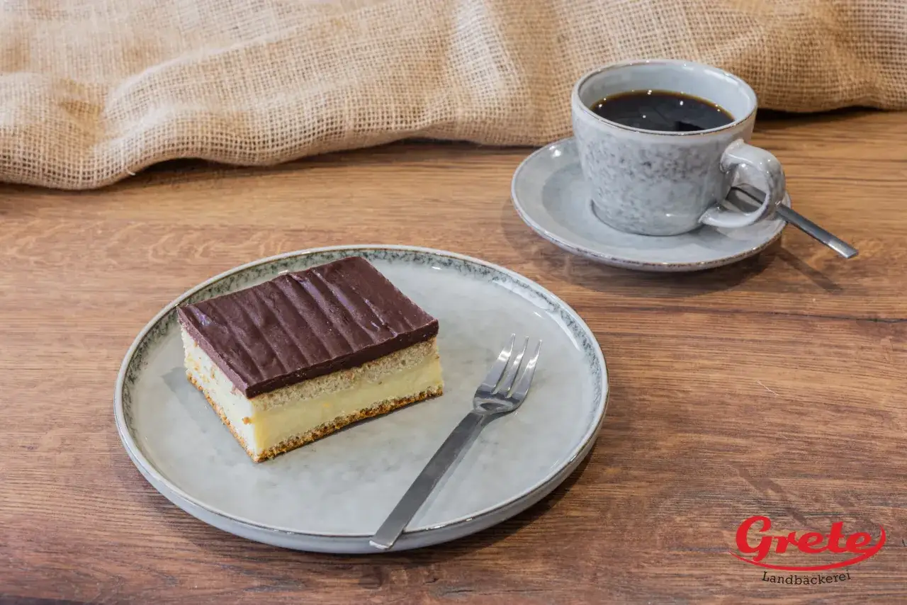Ein St&uuml;ck schokokuchen mit vanillepudding auf einem Teller, daneben eine Tasse Kaffee.