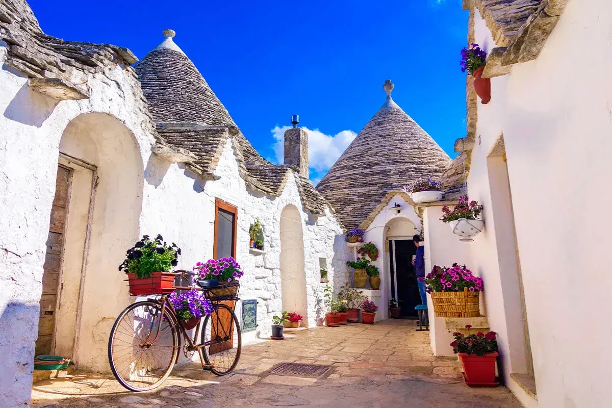 Apulia co zobaczyć: urokliwe uliczki z białymi domkami trulli, kamienne dachy, kwitnące kwiaty i rower ozdobiony bukietami.