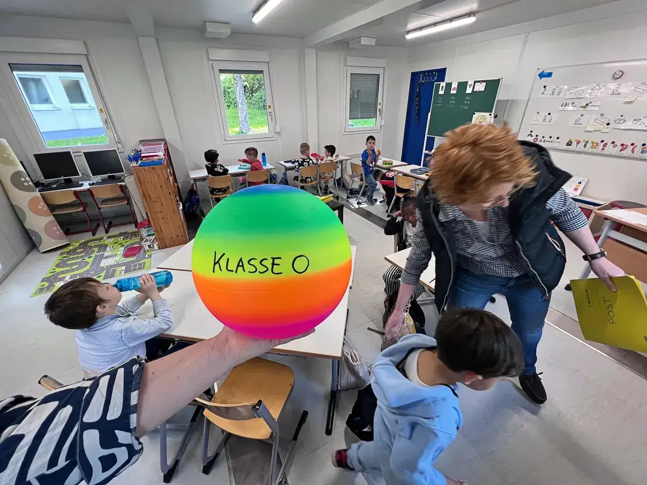 Bunte Ball-Action im Klassenzimmer: Lehrerin und Kinder starten mit lustigen Spielen zum Schulanfang.