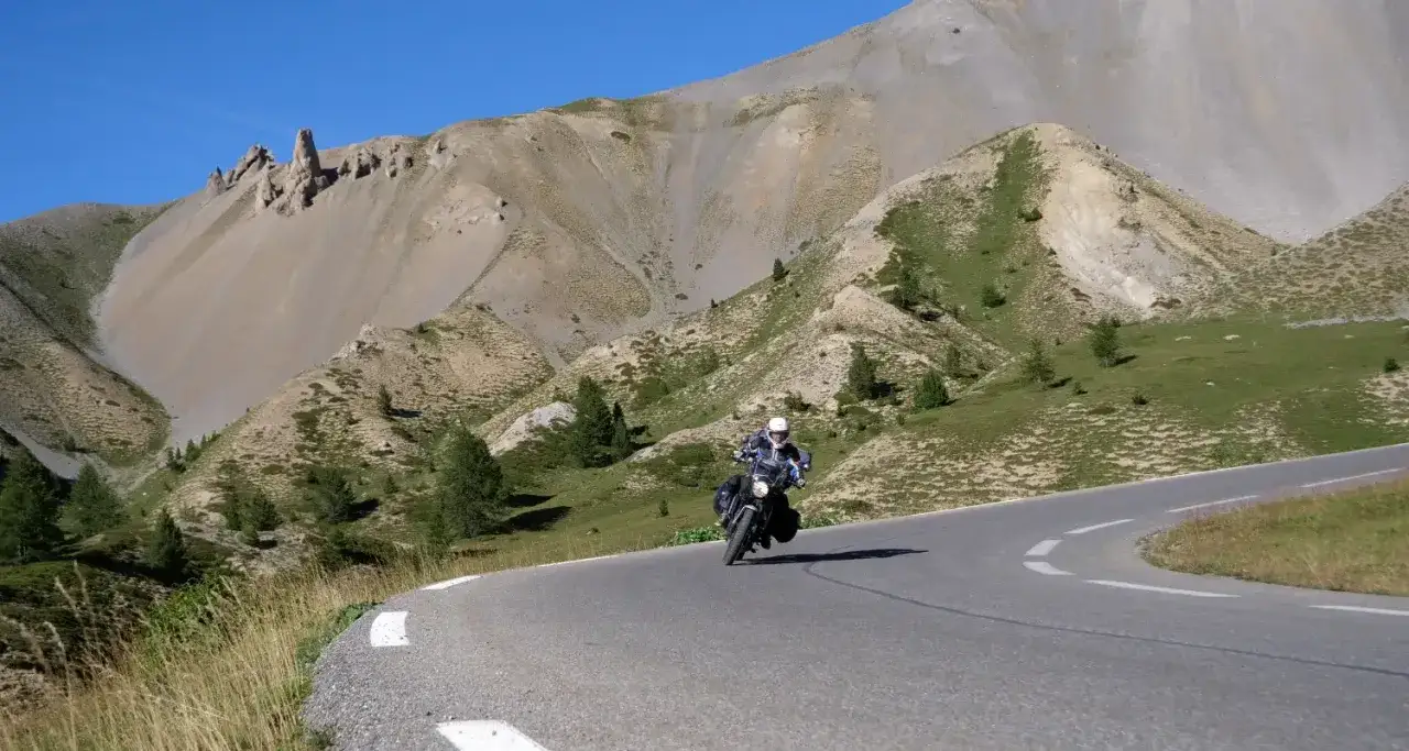 Motociclista percorre la route de grand alpes tra montagne scoscese e verdi pendii.
