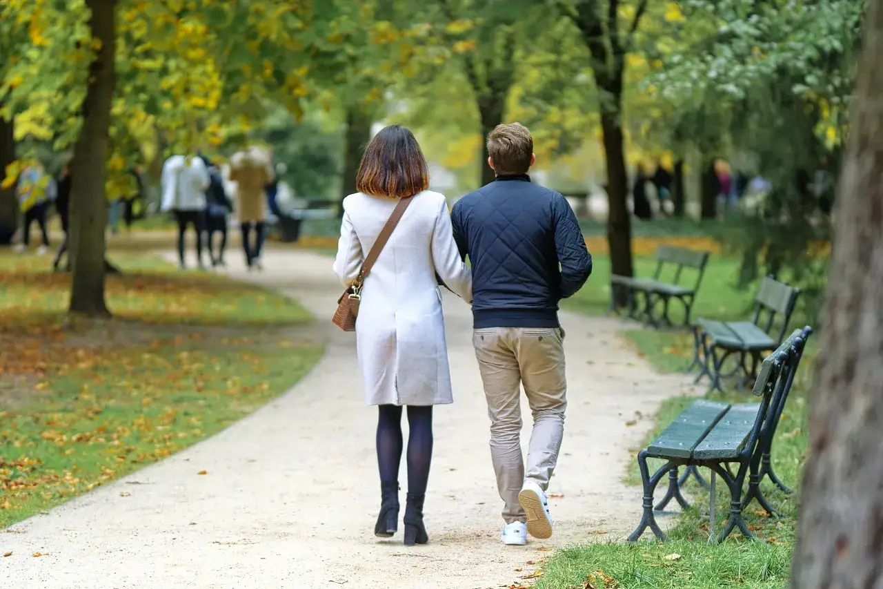 Couple marchant main dans la main dans un parc automnal. Combien de kilomètres faut-il marcher par jour pour profiter de telles promenades ?