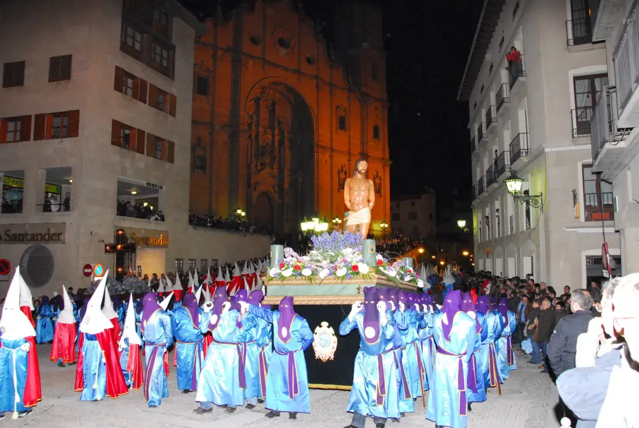 Procesión nocturna en las fiestas de Alcañiz. Hombres con túnicas azules y capirotes portan un paso con una figura de Cristo.