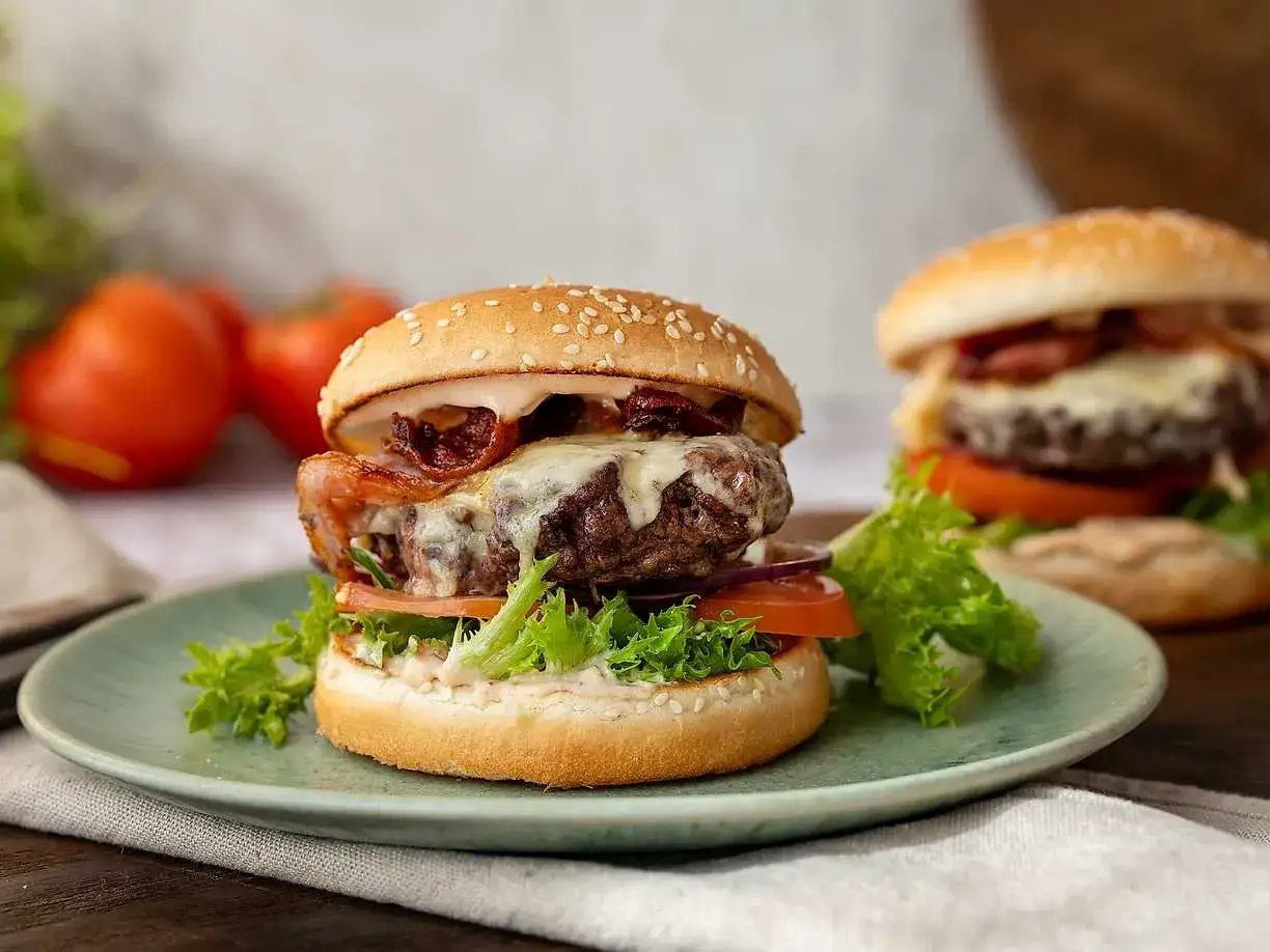 Saftig hamburgare i airfryer med smält ost och krispigt bacon. Serveras på en mintgrön tallrik med färska grönsaker.