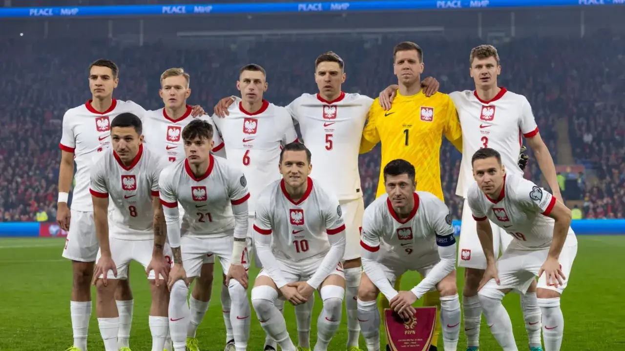 Polscy napastnicy w białych strojach z orłem na piersi, gotowi do walki na boisku.